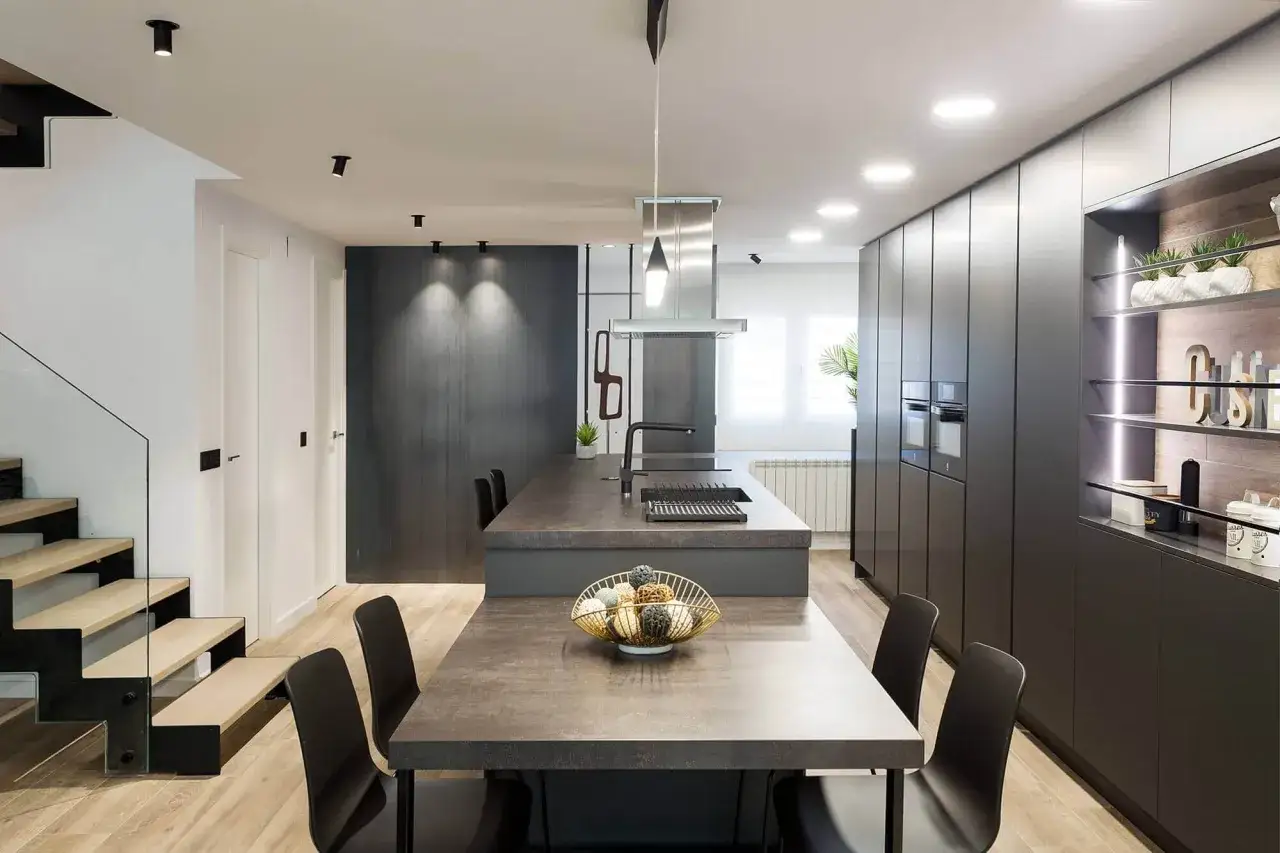 Nowoczesne halogeny sufitowe oświetlają minimalistyczną kuchnię z wyspą i jadalnią. Wnętrze jest eleganckie i funkcjonalne.