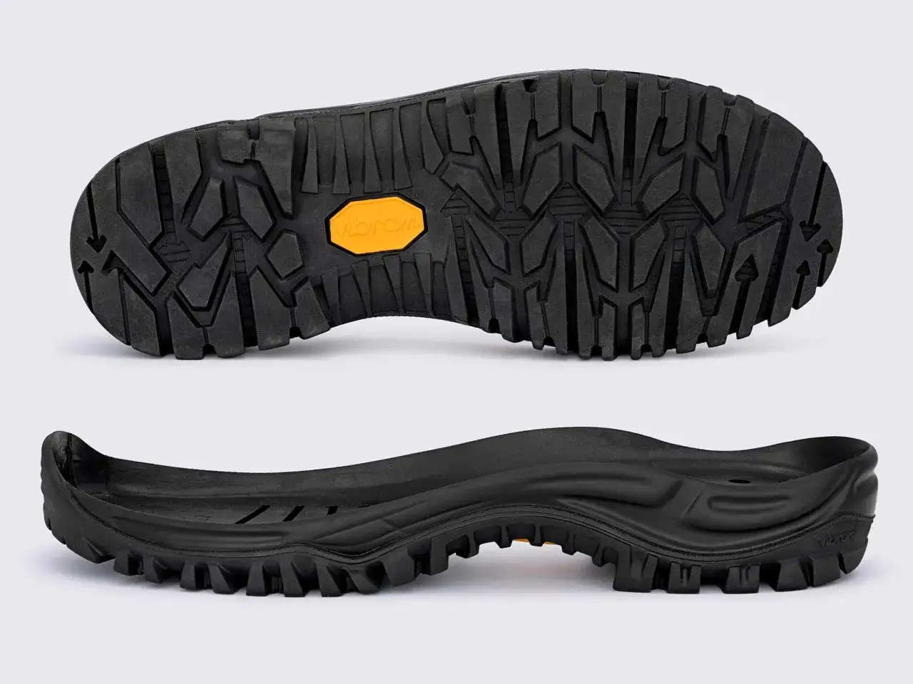 Dwie czarne podeszwy do butów z agresywnym bieżnikiem i pomarańczowym logo Vibram. Idealne na trudny teren.