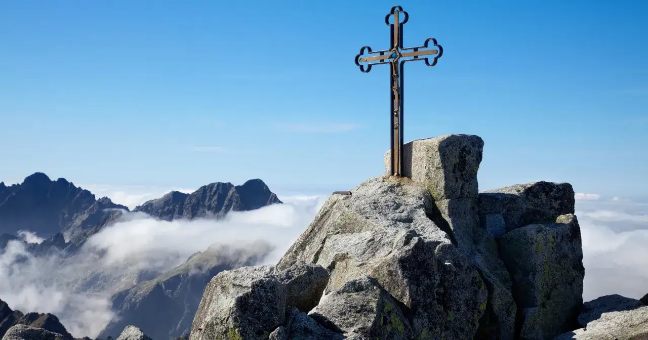 Krzyż na szczycie skalistego wierzchołka. Widok na pasmo górskie i morze chmur. Trasa na Gerlach.