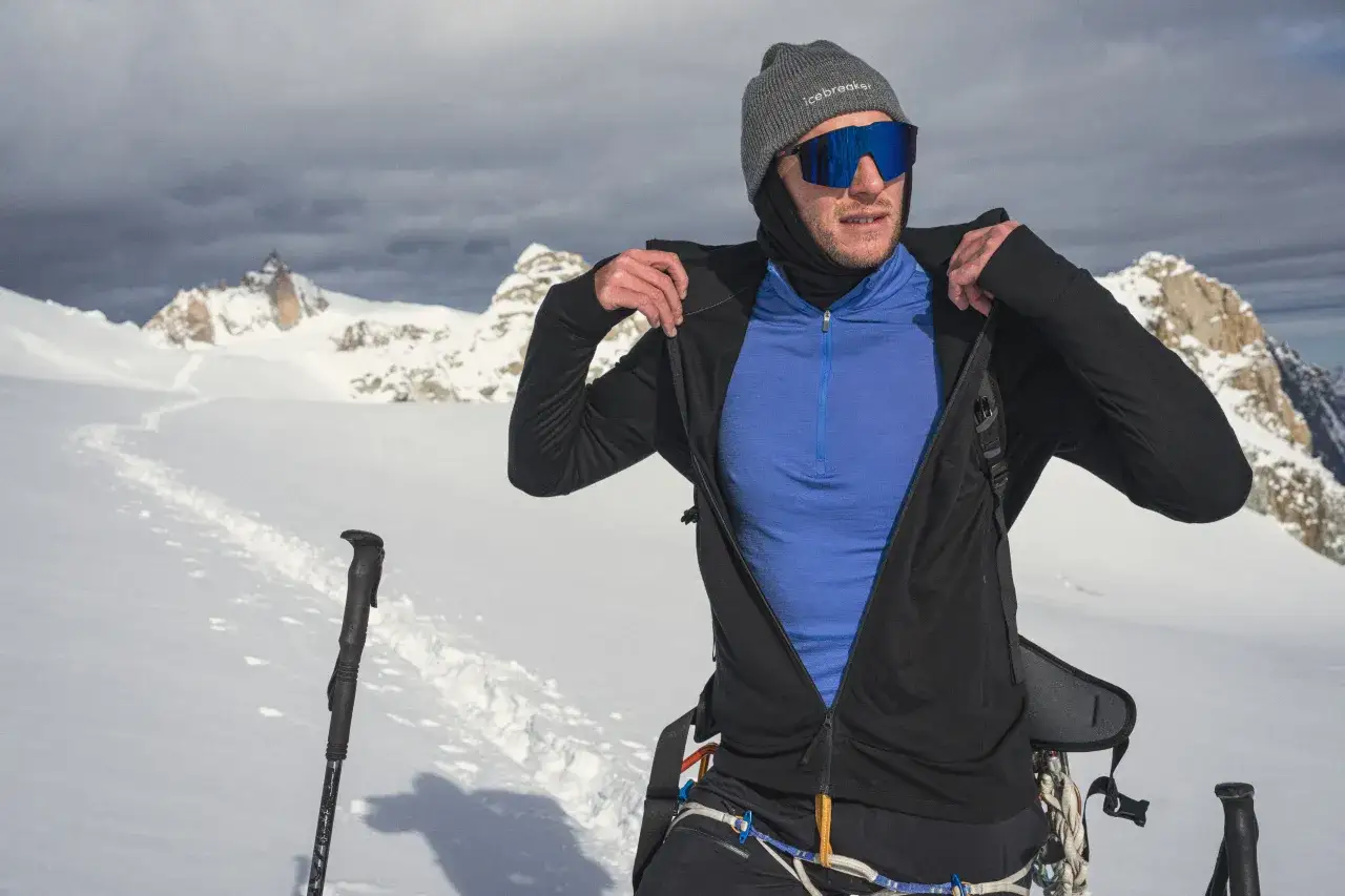 Wspinacz zakłada kurtkę w g&oacute;rach. Wskaz&oacute;wka, jak się ubrać w g&oacute;ry we wrześniu: warstwy, czapka, okulary.