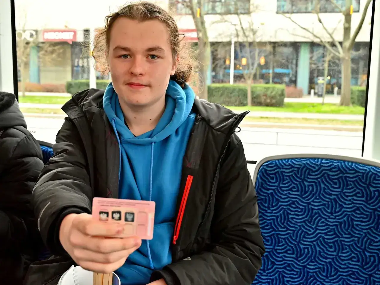 Młody chłopak trzyma legitymację, pokazując, czy we Wrocławiu uczniowie jeżdżą za darmo. Siedzi w pojeździe komunikacji miejskiej.