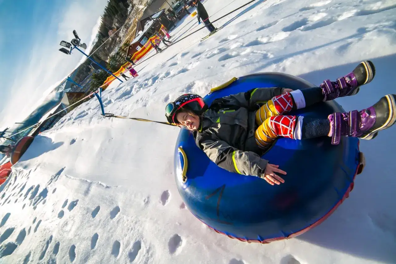 Dziecko na dmuchanej oponce zjeżdża po śniegu. To świetna zabawa na zimowym torze saneczkowym.