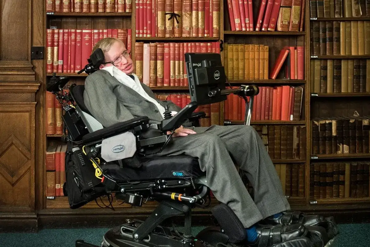 Stephen Hawking, wybitny naukowiec na wózku, siedzi w otoczeniu regałów pełnych książek.