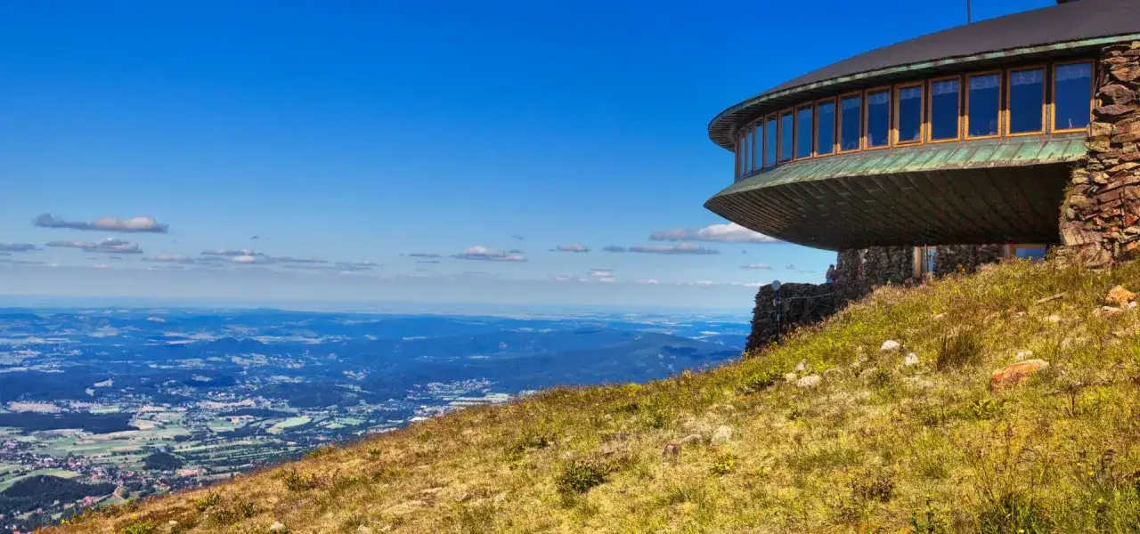Widok z szlaku na Śnieżkę: okrągły budynek z oknami na tle błękitnego nieba i krajobrazu.