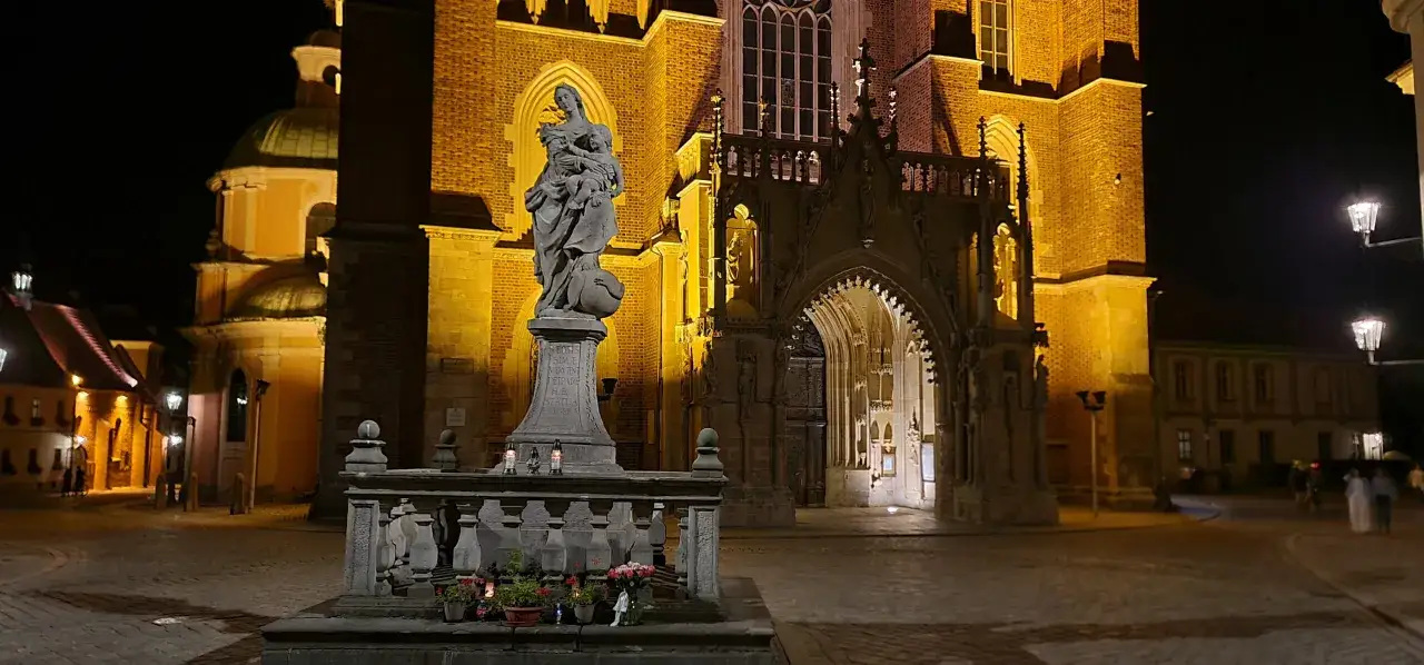 Nocny Wrocław: iluminowana katedra, pomnik i brukowany plac. Idealne miejsce na wieczorne spacery i odkrywanie wrocławskich atrakcji dla dorosłych.