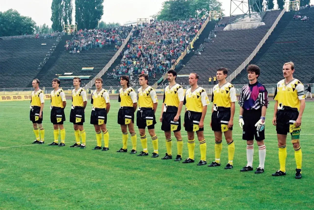 GKS Katowice piłkarze w żółtych strojach stoją w szeregu na murawie stadionu, przed trybunami pełnymi kibiców.
