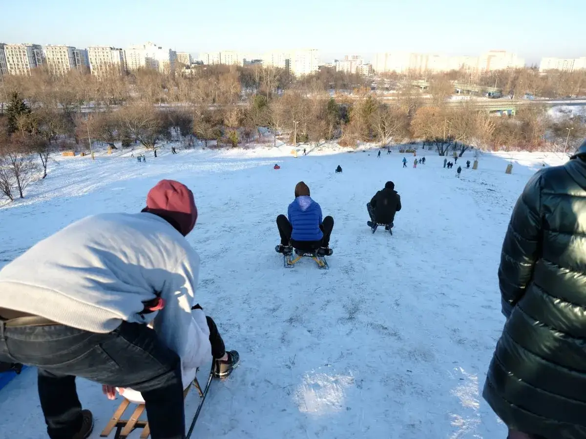 Zima zachęca, gdzie na sanki! Ludzie zjeżdżają ze śnieżnej g&oacute;rki, ciesząc się mroźnym dniem.