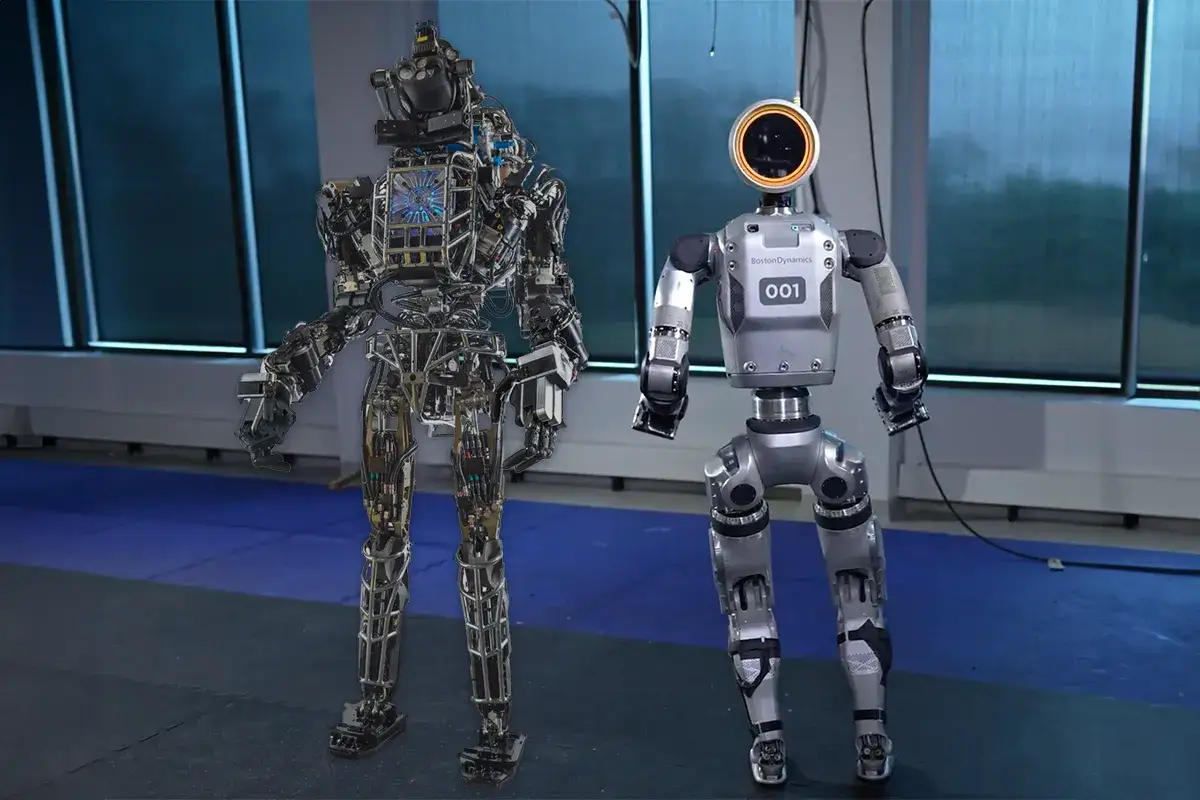 Dwa roboty humanoidalne, jeden z widocznym szkieletem i kablami, drugi gładki i srebrny z numerem 001.