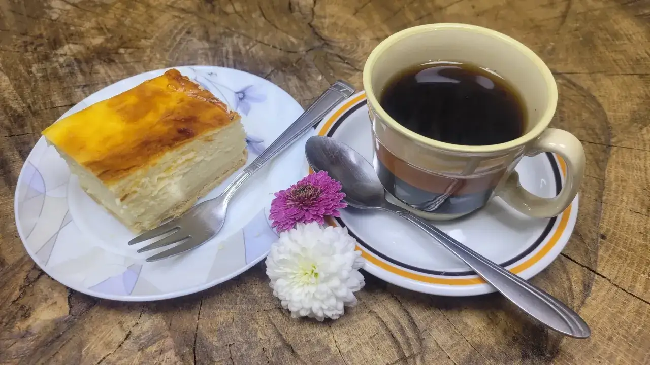 Kawa i kawałek sernika na talerzyku, obok kwiaty. Idealny zestaw, zastanawiam się jaki aromat do sernika byłby najlepszy.