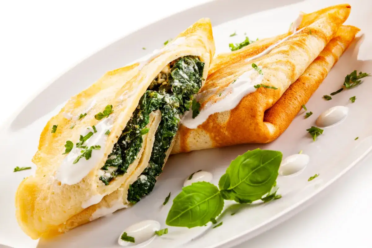 Naleśniki ze szpinakiem i serem, polane sosem, idealne na obiad. Udekorowane natką pietruszki i bazylią.