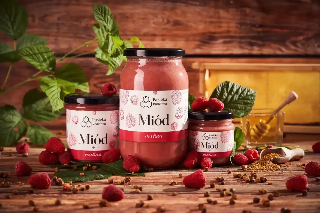 Reklamowa fotografia miodu malinowego z malinami i plastrem miodu.