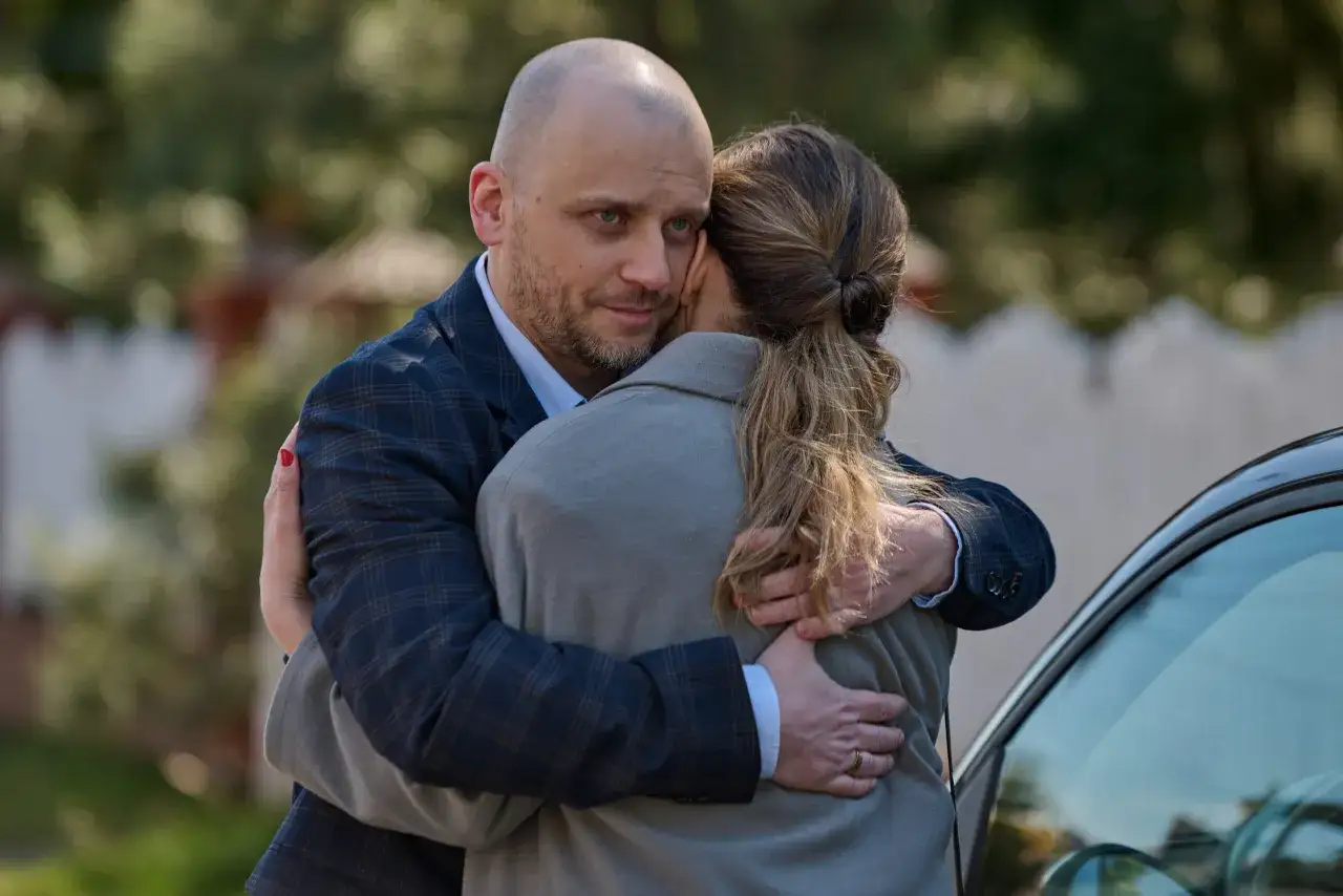 Mężczyzna obejmuje kobietę, patrząc wprost w obiektyw. Czy ukryta prawda dalej jest nagrywana w tym czułym uścisku?