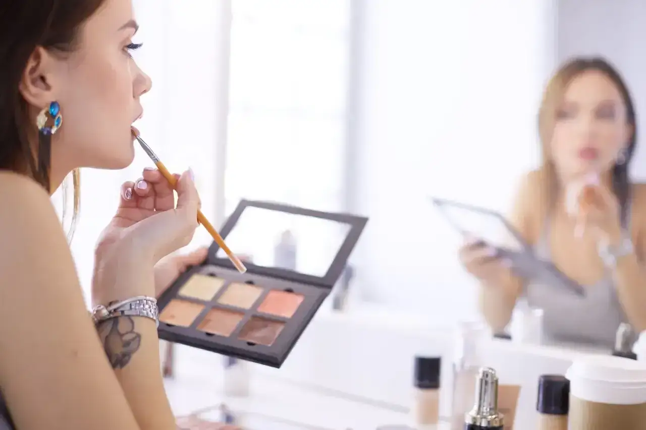 Wizażystka nakłada makijaż, zastanawiając się, ile zarabia. W tle druga kobieta też się maluje.
