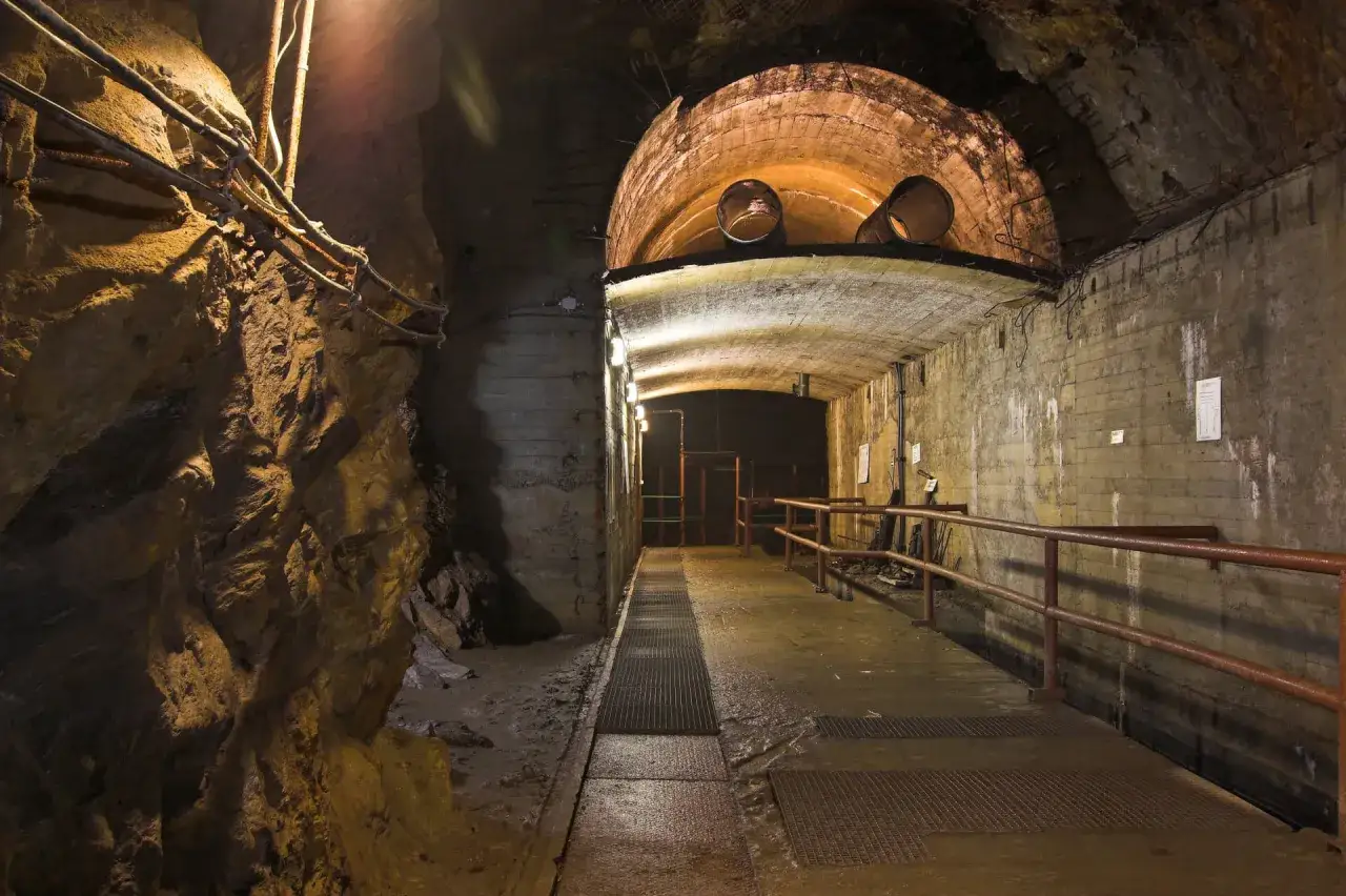 Podziemny korytarz z betonowymi ścianami i łukowym sklepieniem, oświetlony lampami. To jedno z mało znanych miejsc na Dolnym Śląsku, skrywające tajemnice.