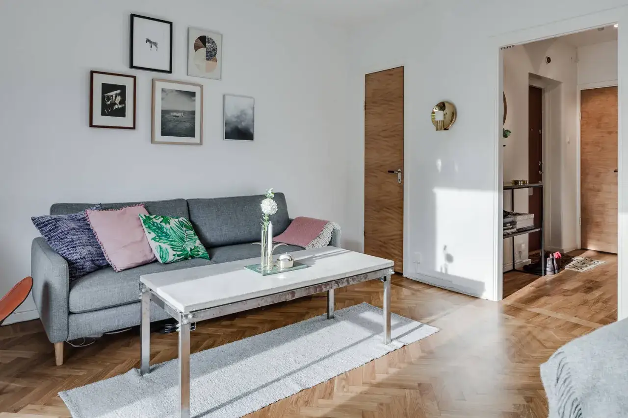 Jak urządzić małe mieszkanie 38 m? Jasny salon z szarą kanapą, stolikiem i galerią obrazów na ścianie.