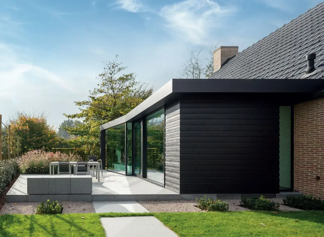 Nowoczesna bryła domu z czarnym akrylem do elewacji, dużymi przeszkleniami i tarasem z meblami ogrodowymi.