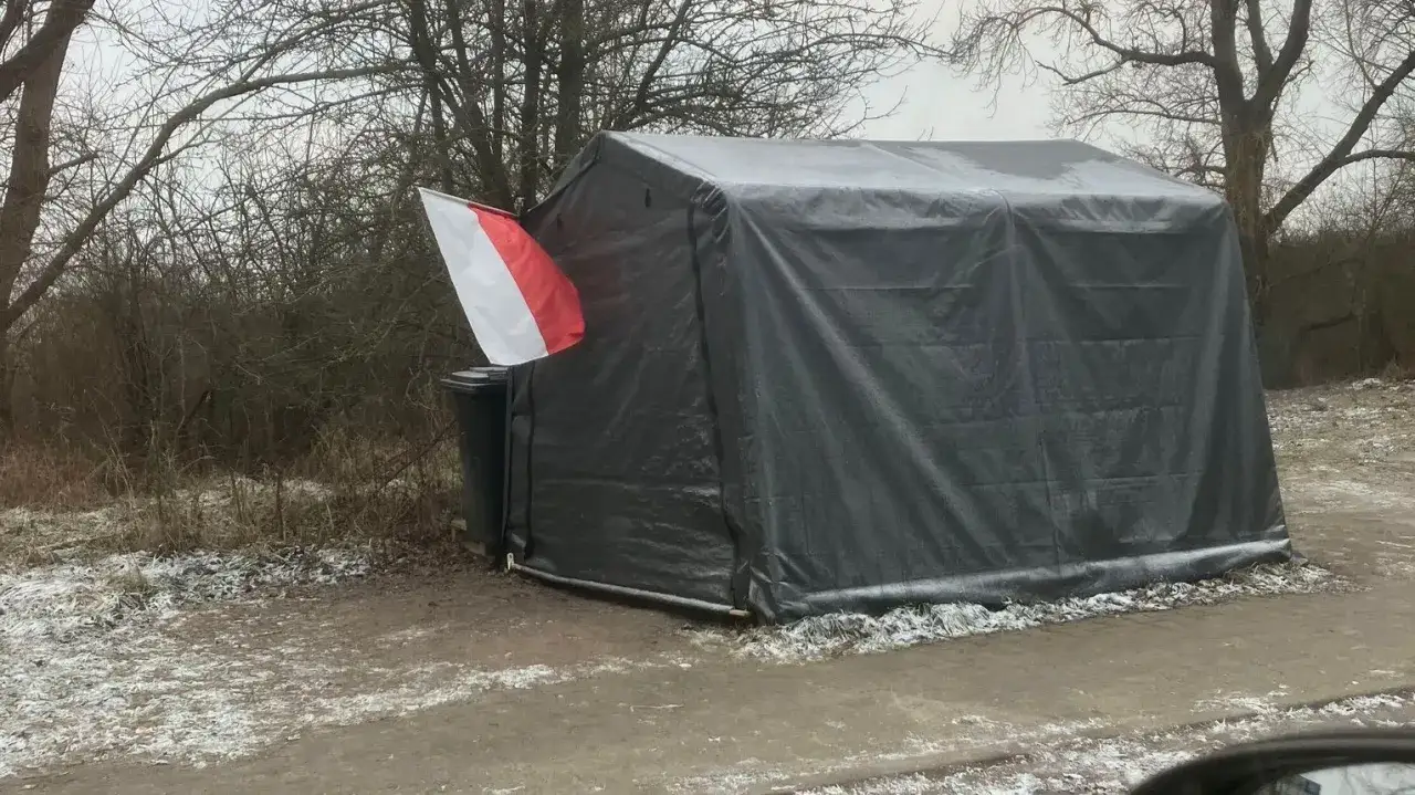 Czarny namiot z polską flagą, gotowy do rozłożenia. Zimowy krajobraz i śnieg wok&oacute;ł.