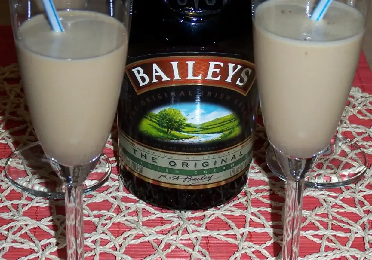 Dwa kieliszki z kremowym drinkiem z likierem kawowym i mlekiem, obok butelka Baileys.