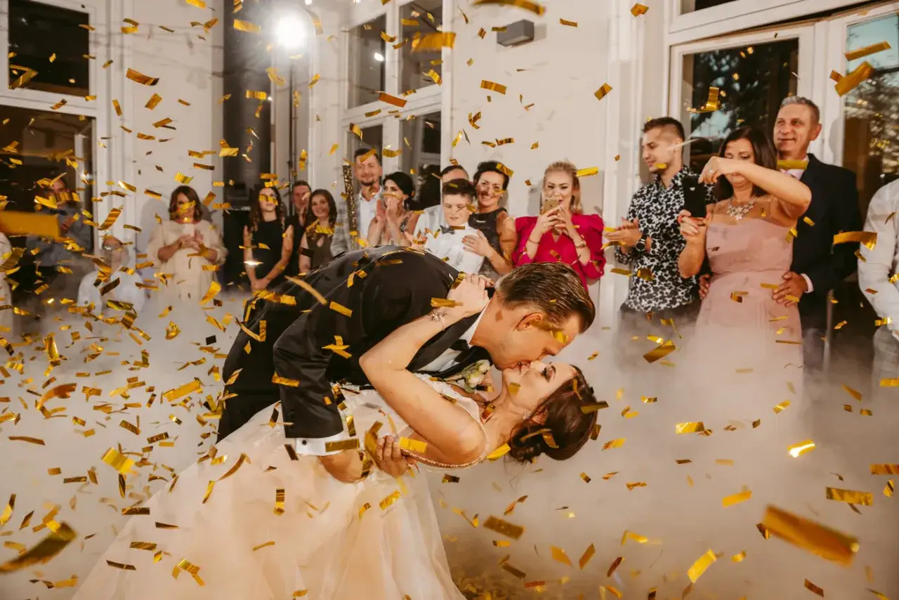 Para młoda całuje się w chmurze dymu i złotego konfetti, podczas pierwszych tańców weselnych.