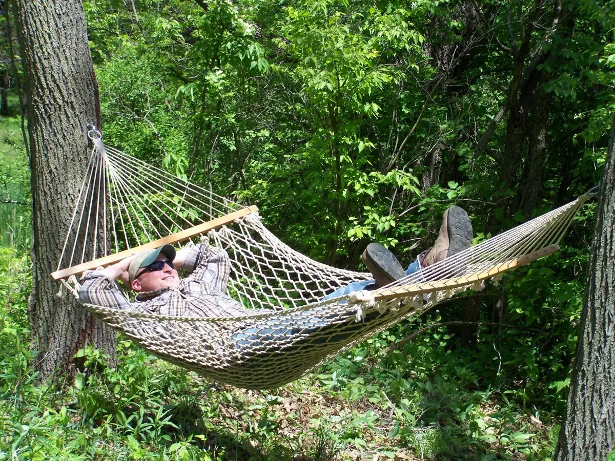 Mężczyzna relaksuje się w hamaku zawieszonym na drzewie. Prosty spos&oacute;b, jak zawiesić hamak na drzewie, by cieszyć się naturą.