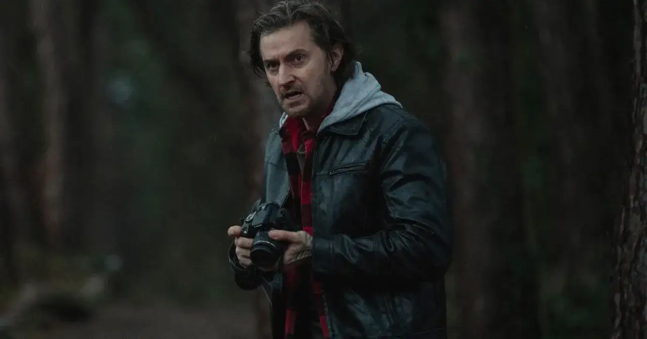 Mężczyzna w sk&oacute;rzanej kurtce i flanelowej koszuli trzyma aparat. Czy to prezent od losu, kt&oacute;ry uchwyci coś niezwykłego w lesie?