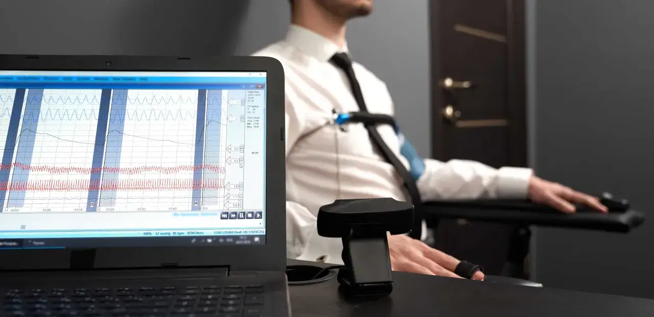 Badanie wykrywaczem kłamstw w Warszawie. Na ekranie laptopa wykresy fizjologiczne, mężczyzna w białej koszuli z czujnikami.