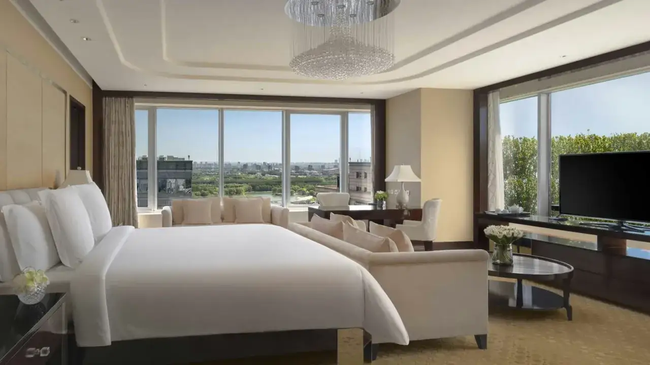 Luksusowy apartament z widokiem na miasto, przypominający najdroższy hotel na świecie. Ogromne okna, kryształowy żyrandol i wygodne meble.