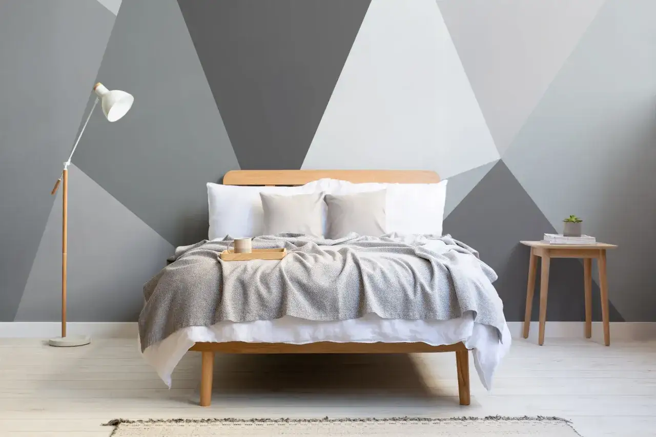 Nowoczesna sypialnia z łóżkiem, lampą i stolikiem. Ściana za łóżkiem ozdobiona geometrycznym wzorem, tworzącym efekt tapety wypukłej.