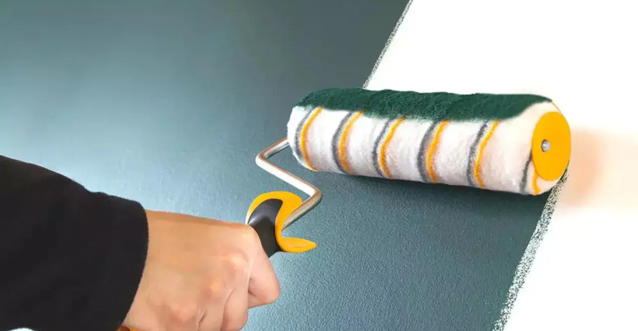 Dłoń trzyma wałek do malowania, który maluje białą ścianę na ciemnozielony kolor. To pokazuje, jak wybrać wałek do malowania.