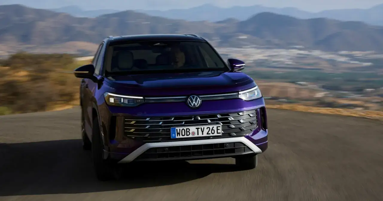 Fioletowy Tayron VW pędzi po krętej drodze, otoczony malowniczymi wzg&oacute;rzami.
