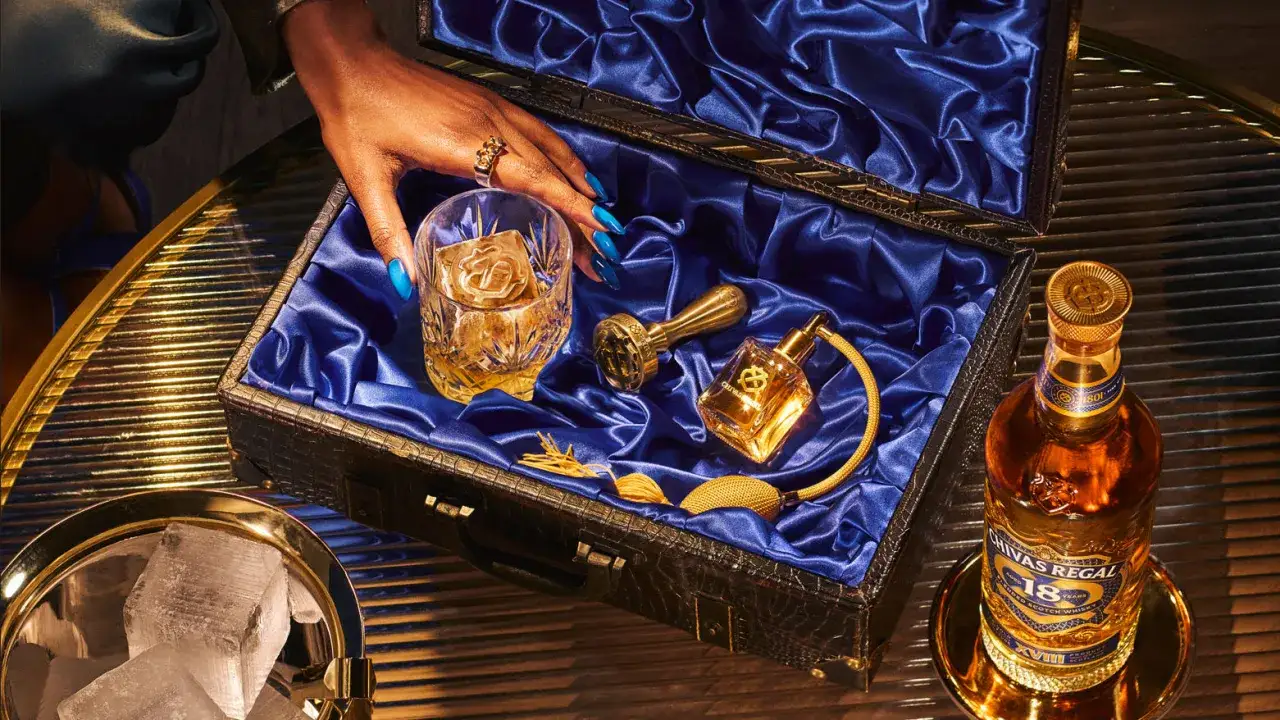 Skutki trzymania butelki whisky w nasłonecznionym miejscu: blaknięcie etykiet. Zestaw z whisky, lodem i złotymi akcesoriami.