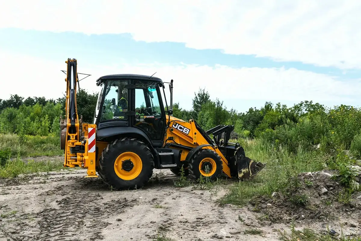 Żółta koparko-ładowarka JCB na placu budowy. Czy na koparkę trzeba mieć uprawnienia? Tak, do obsługi tego sprzętu potrzebne są odpowiednie kwalifikacje.