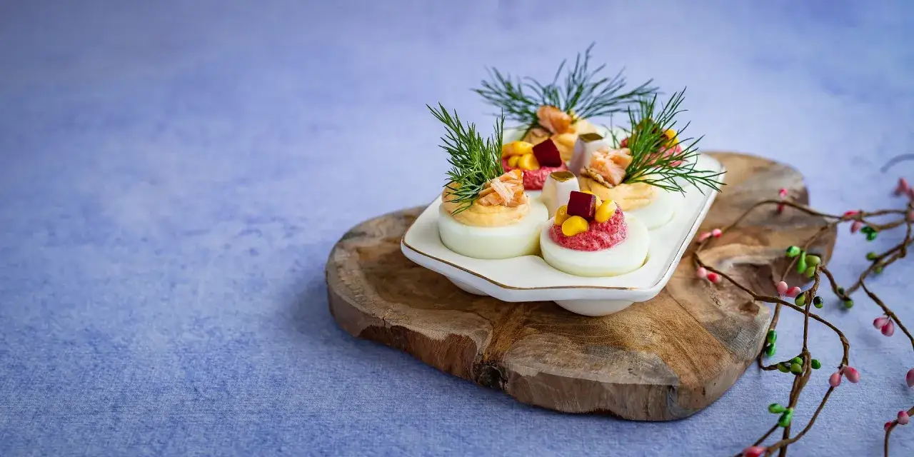 Eleganckie jajka faszerowane z łososiem, ozdobione koperkiem i warzywami, na drewnianej desce.