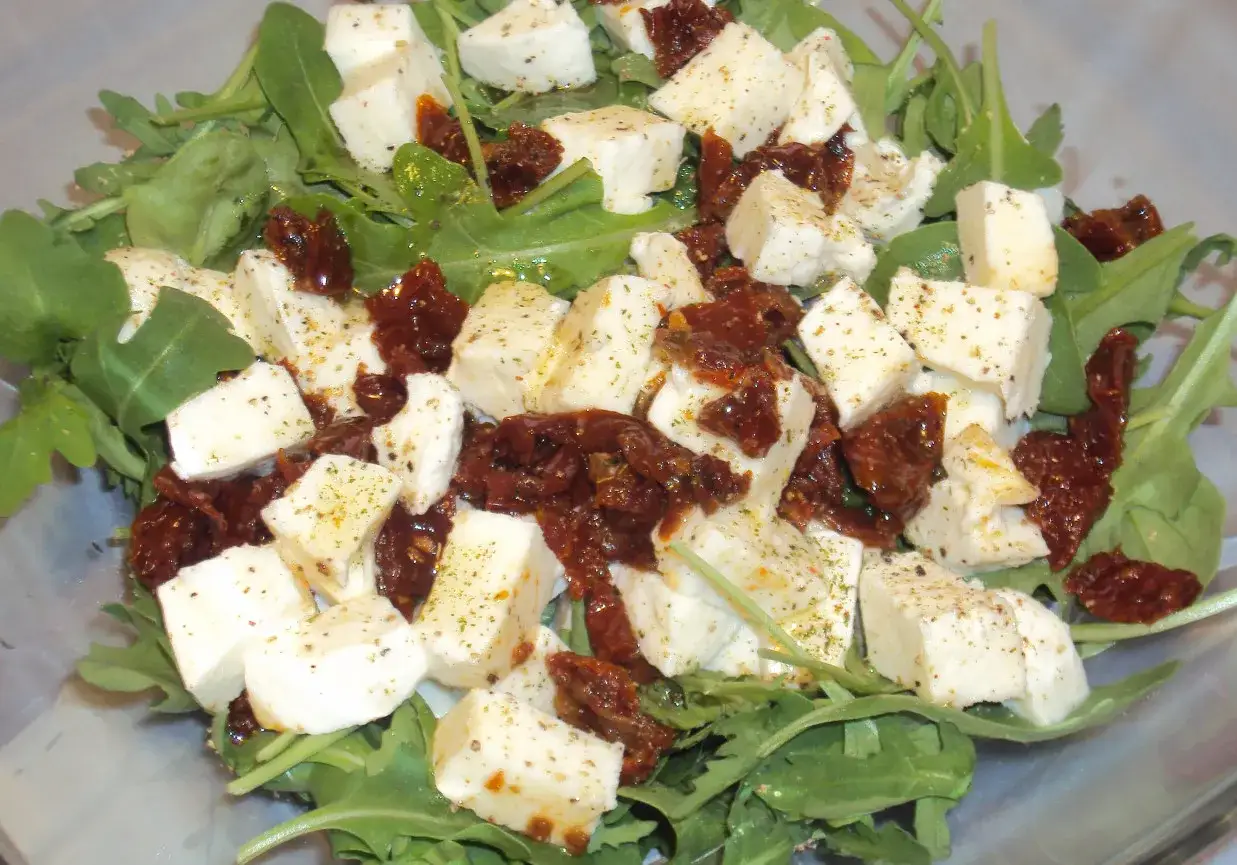 Sałatka z rukolą, kawałkami mozzarelli i suszonymi pomidorami, doprawiona ziołami.