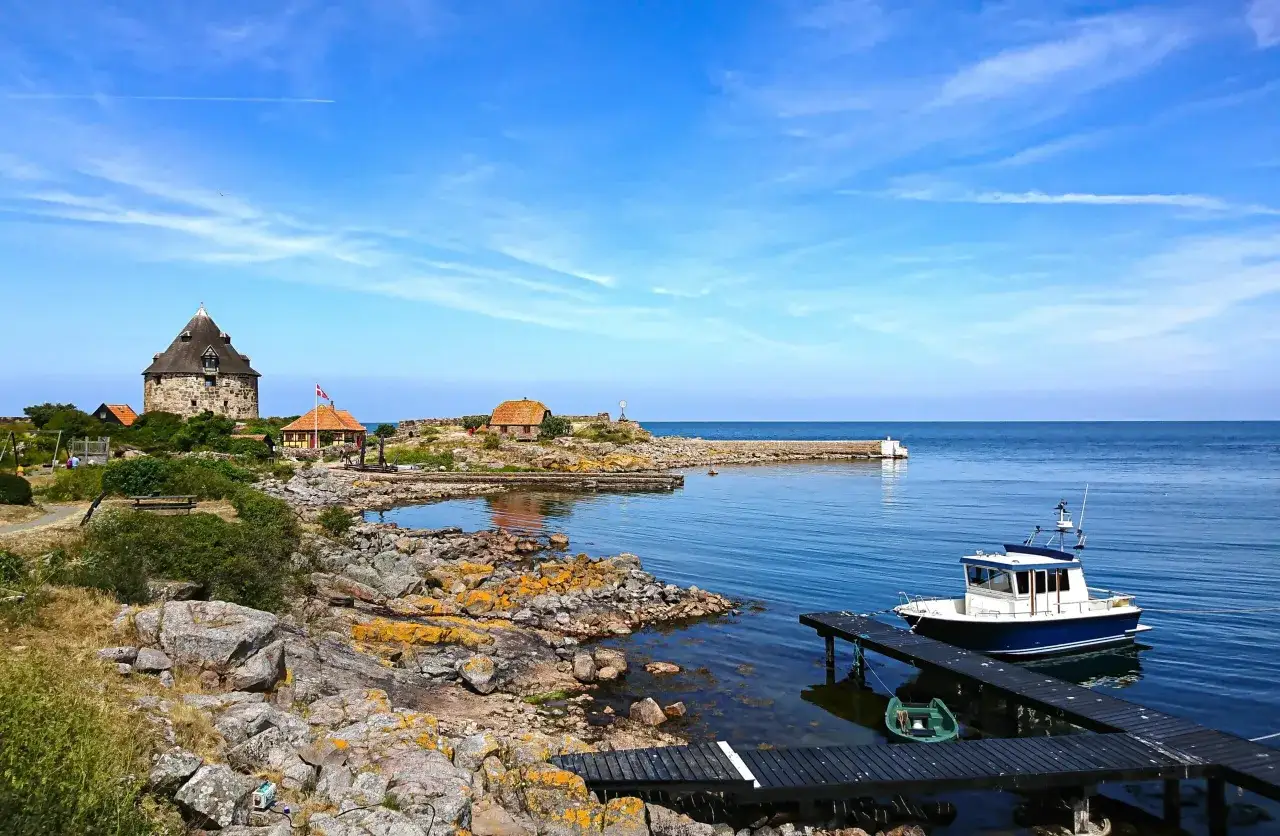 Kamienna wieża i domki na skalistej duńskiej wyspie na Bałtyku. Łódź cumuje przy drewnianym pomoście.