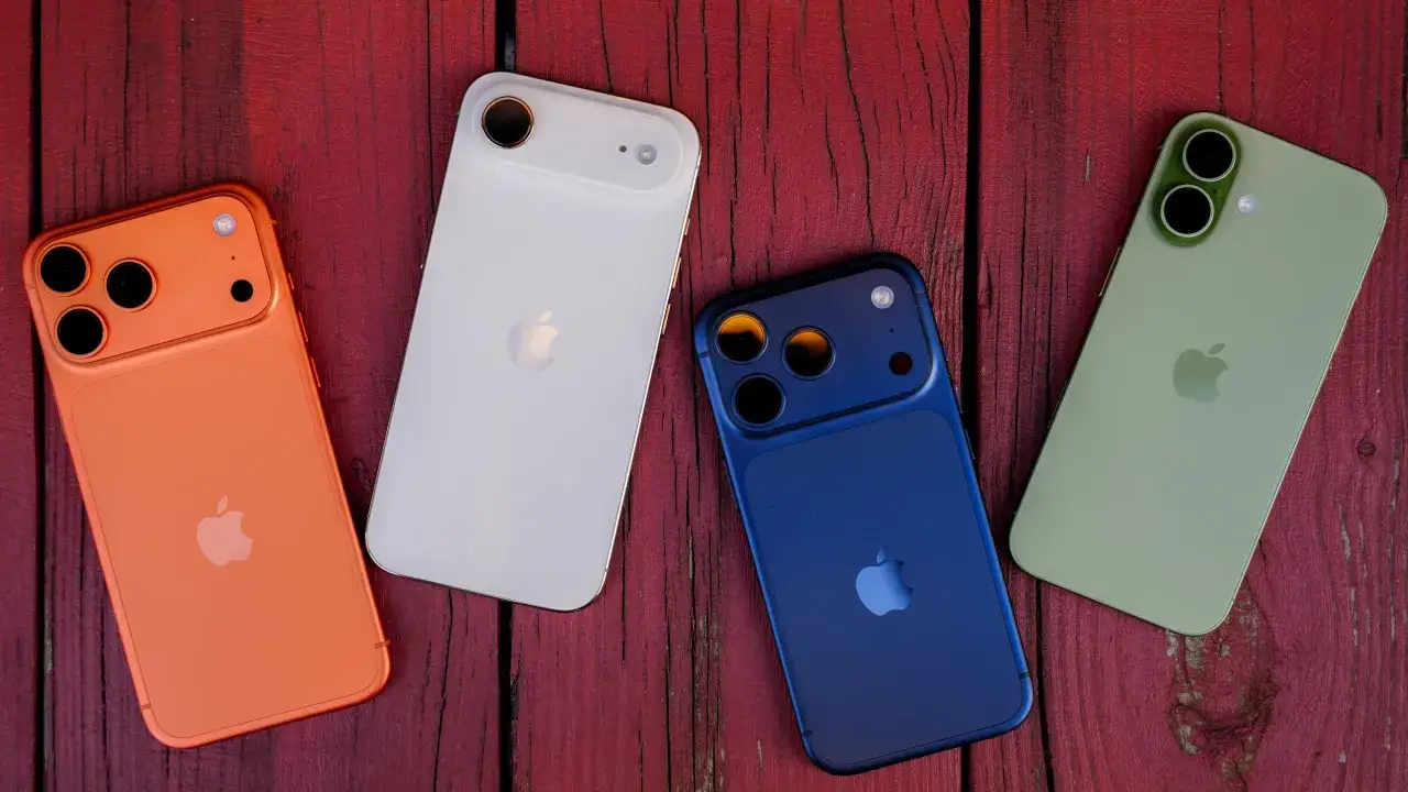 Pomarańczowy, biały, niebieski i zielony iPhone leżą obok siebie na czerwonym, drewnianym tle. To świetne por&oacute;wnanie modeli iPhone.