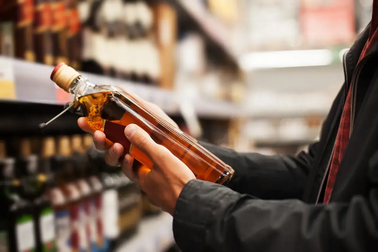Ręce trzymają butelkę bursztynowego alkoholu, zastanawiając się, ile alkoholu z Ukrainy kupić.