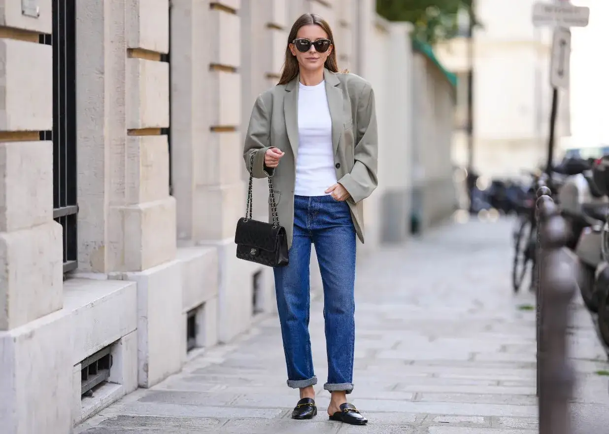 Kobieta w luźnej marynarce i białym t-shircie pod marynarkę, jeansach i czarnej torebce na łańcuszku.