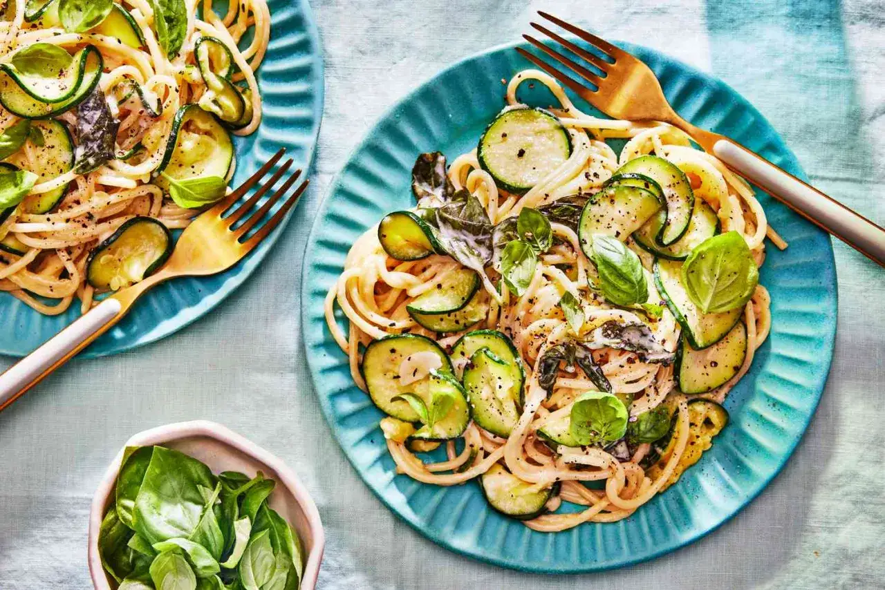 Pyszny makaron z cukinii, podany na turkusowych talerzach, ozdobiony świeżą bazylią i złotymi widelcami.