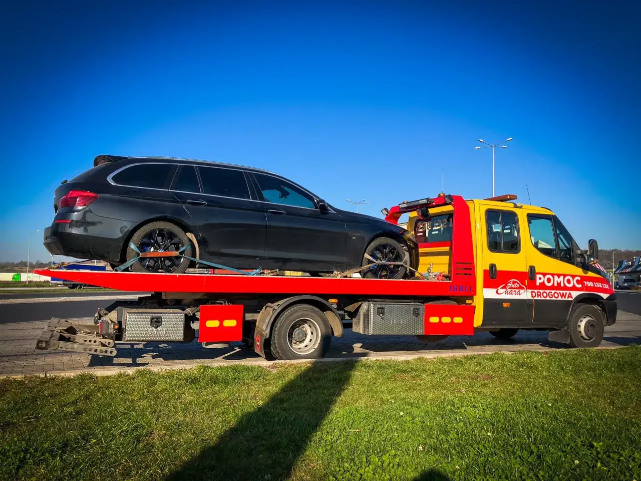 Auto pomoc drogowa transportuje czarny samoch&oacute;d. Gdy auto nie chce odpalić, to znak, że potrzebna jest pomoc.