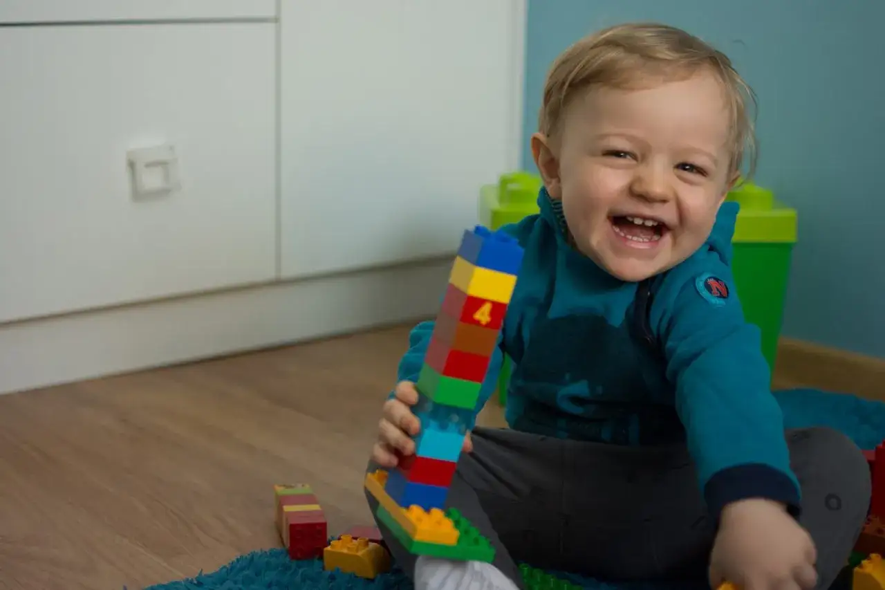 Dziecko z uśmiechem budujące wieżę z klock&oacute;w LEGO