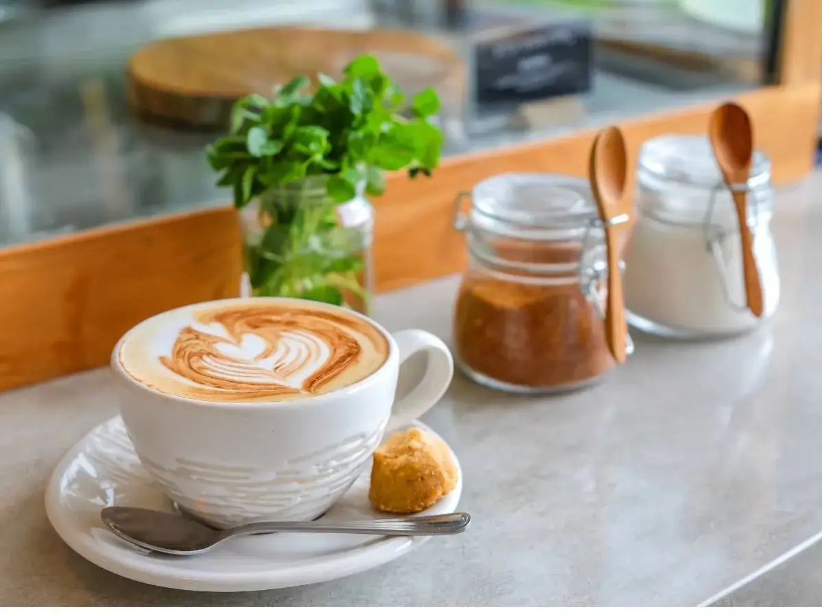 Aromatyczna kawa latte z sercem na piance, ciasteczko i cukier &ndash; to początek pięknej historii kawy.