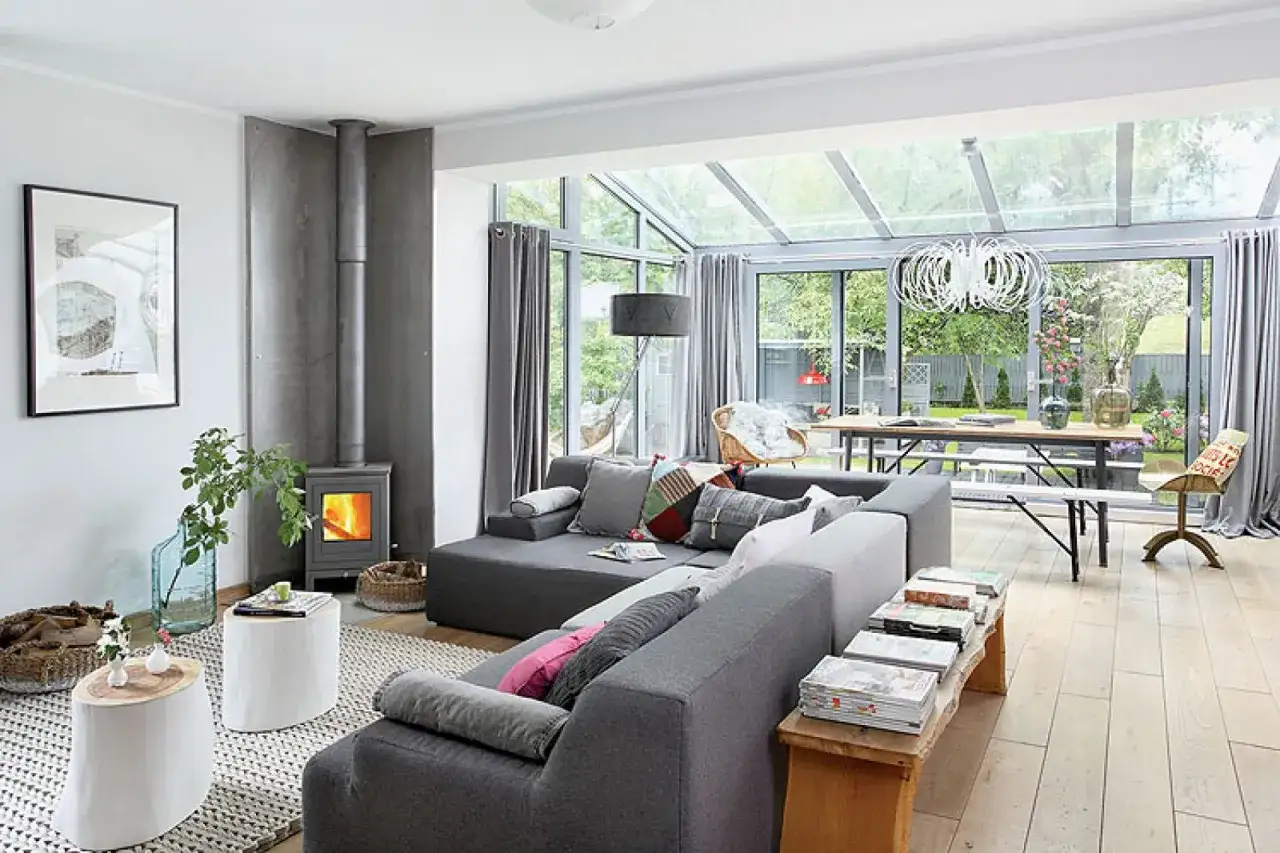 Przytulny salon z kominkiem i przeszklonym dachem, idealny do relaksu. Ten **dom w stylu holenderskim** zachwyca jasnym wnętrzem i widokiem na ogród.