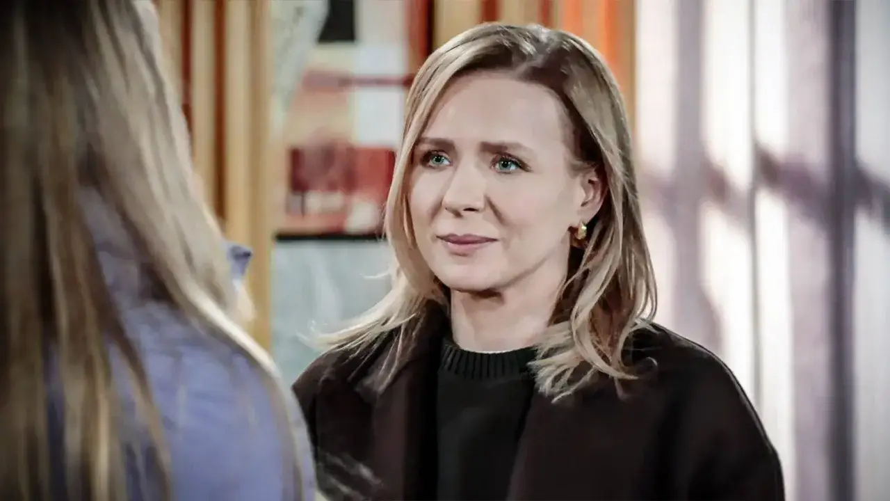 Blondynka z niebieskimi oczami, w brązowym płaszczu, patrzy z lekkim uśmiechem, jakby wspominała tęsknota za pierwszą miłością.