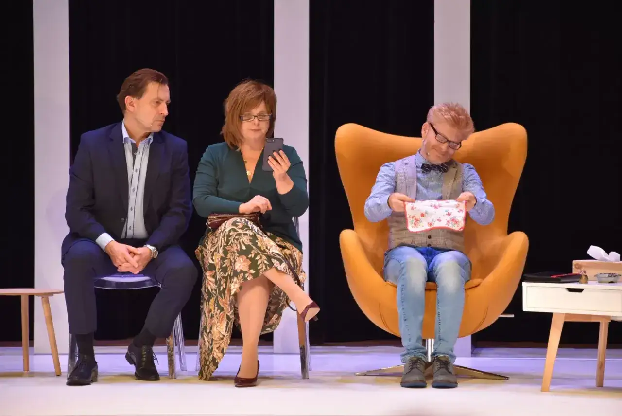 Na scenie, w ramach cudowna terapia spektakl, siedzą trzej aktorzy. Jeden z nich, w pomarańczowym fotelu, trzyma chusteczkę.