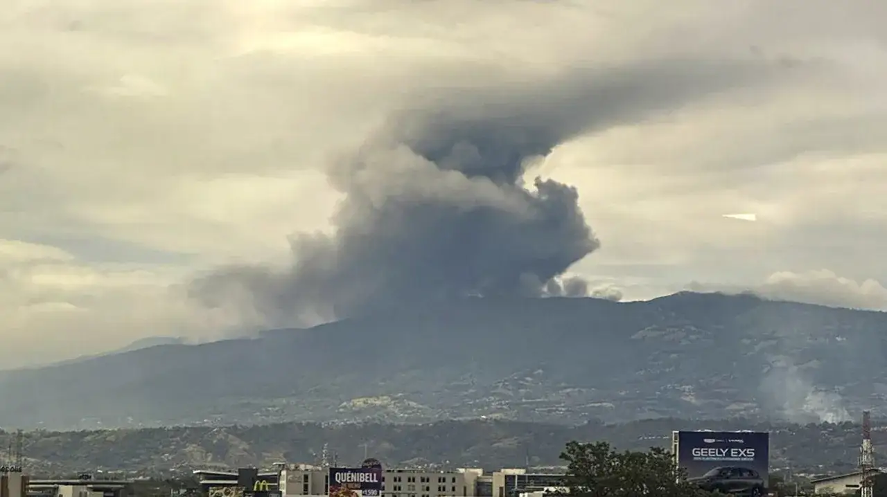 Dym z wulkanu nad Kostaryką. Czy Kostaryka jest bezpieczna? Wulkaniczna chmura unosi się nad górami, a w oddali widać zabudowania.