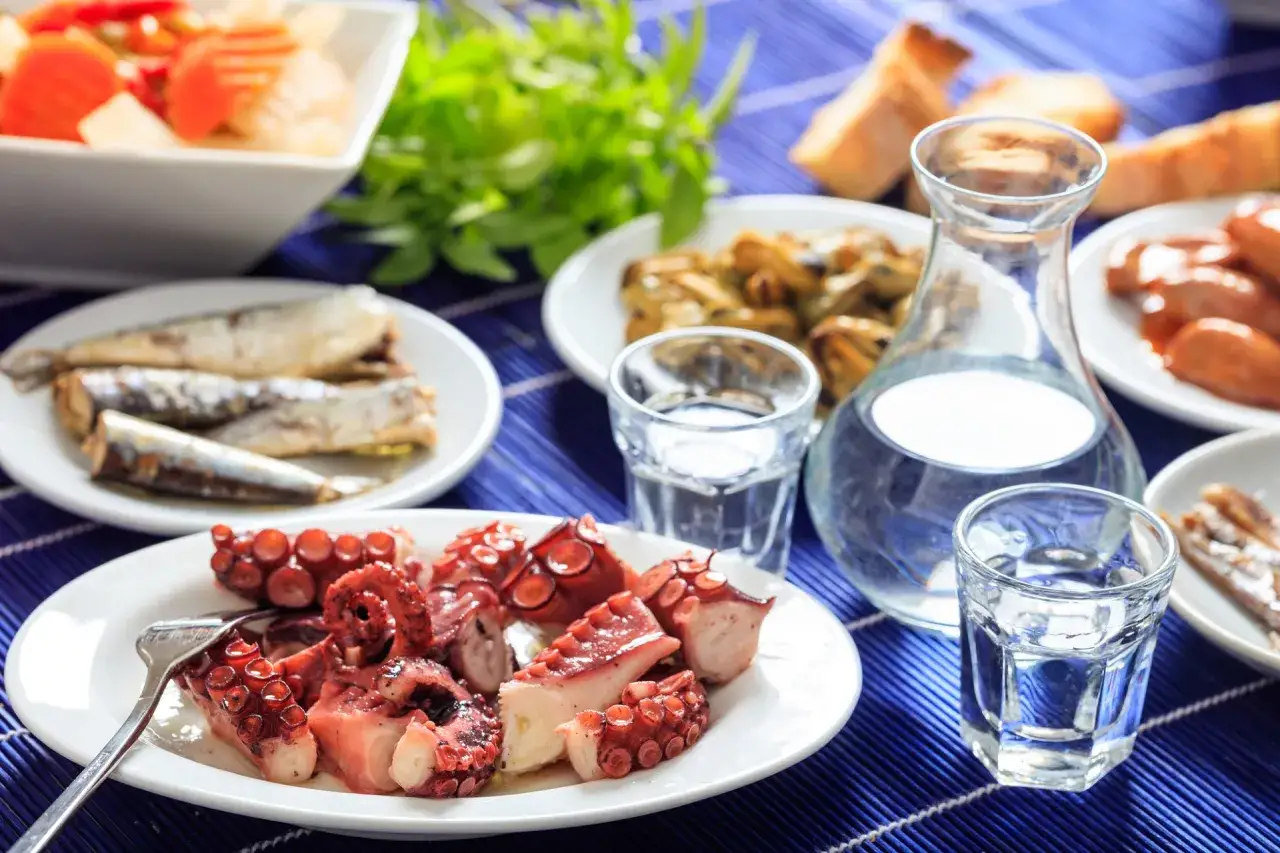 Ouzo jak pić? Na stole grillowana ośmiornica, sardynki, mule i kieliszki z wodą. Idealne greckie meze.