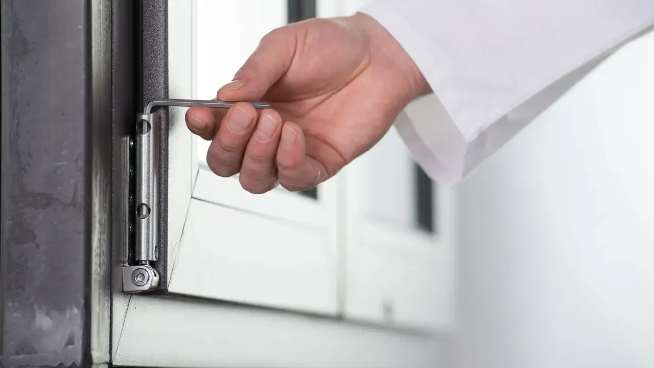 Regulacja docisku skrzydła okiennego kluczem imbusowym krok po kroku. Dłoń z kluczem imbusowym przy zawiasie okna.