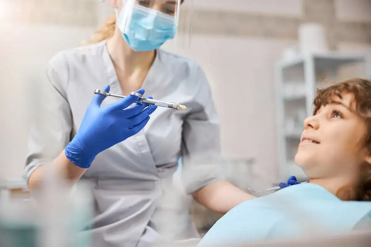 Dentystka w niebieskich rękawiczkach przygotowuje znieczulenie miejscowe dla uśmiechniętego chłopca.