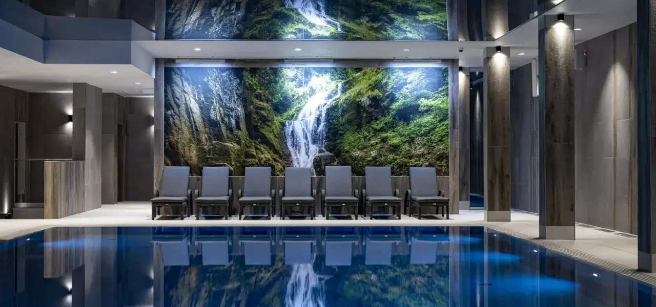 Relaks przy basenie w hotelu w Szklarskiej Porębie. Woda odbija malowniczy wodospad na ścianie.